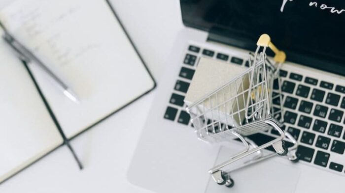 A laptop and a miniature shopping cart symbolizing how to sell online